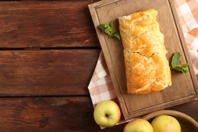 Photo of Delicious strudel with apples and mint on wooden table, flat lay. Space for text