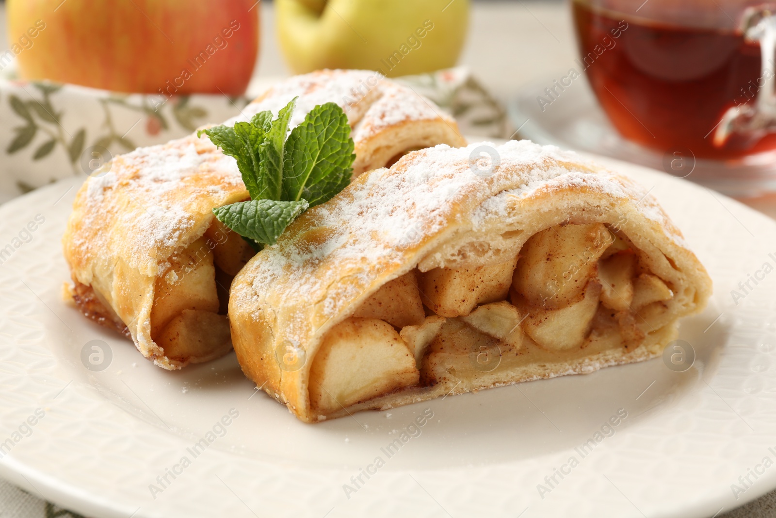 Photo of Pieces of tasty apple strudel with powdered sugar and mint on table, closeup