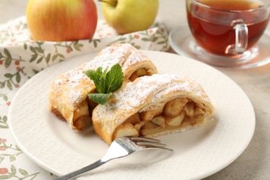 Pieces of tasty apple strudel with powdered sugar and mint on light table, closeup