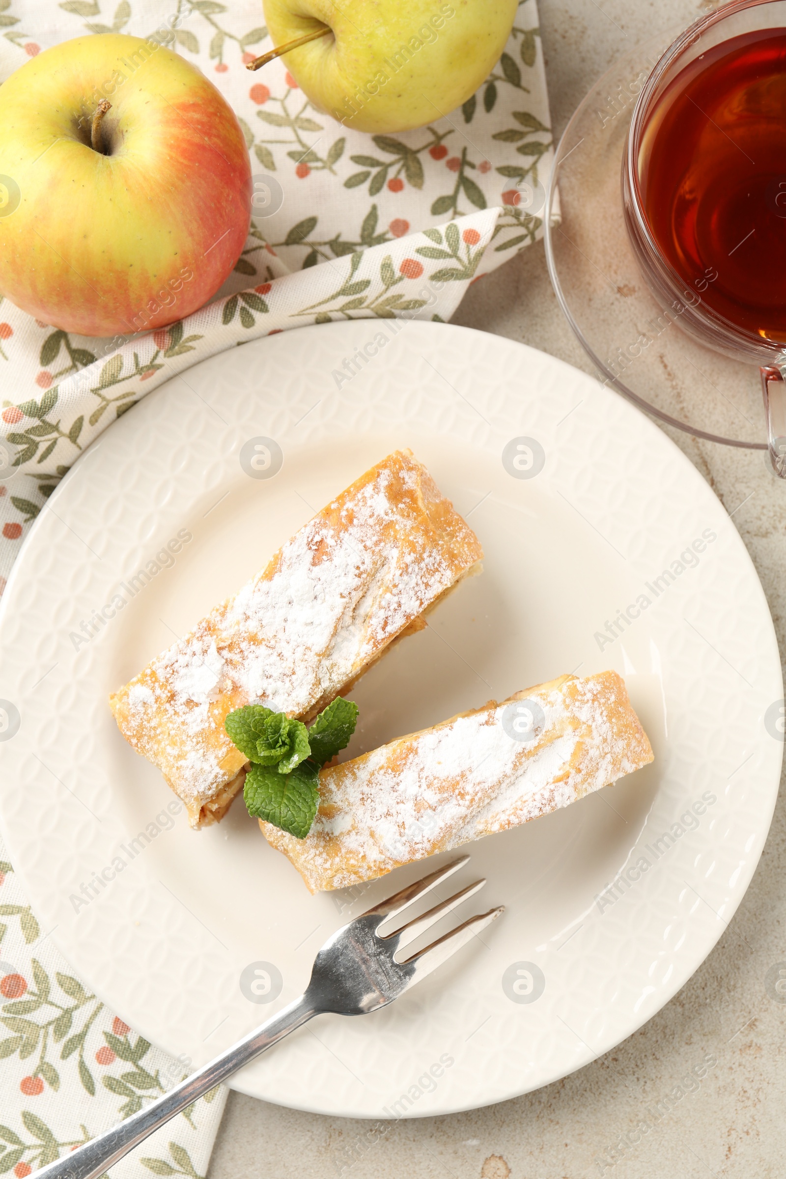 Photo of Pieces of tasty apple strudel with powdered sugar and mint on grey textured table, flat lay