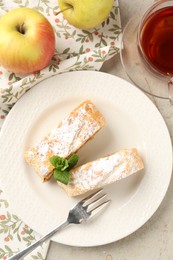 Photo of Pieces of tasty apple strudel with powdered sugar and mint on grey textured table, flat lay