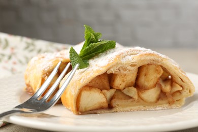 Photo of Pieces of tasty apple strudel with powdered sugar, mint and fork on table, closeup