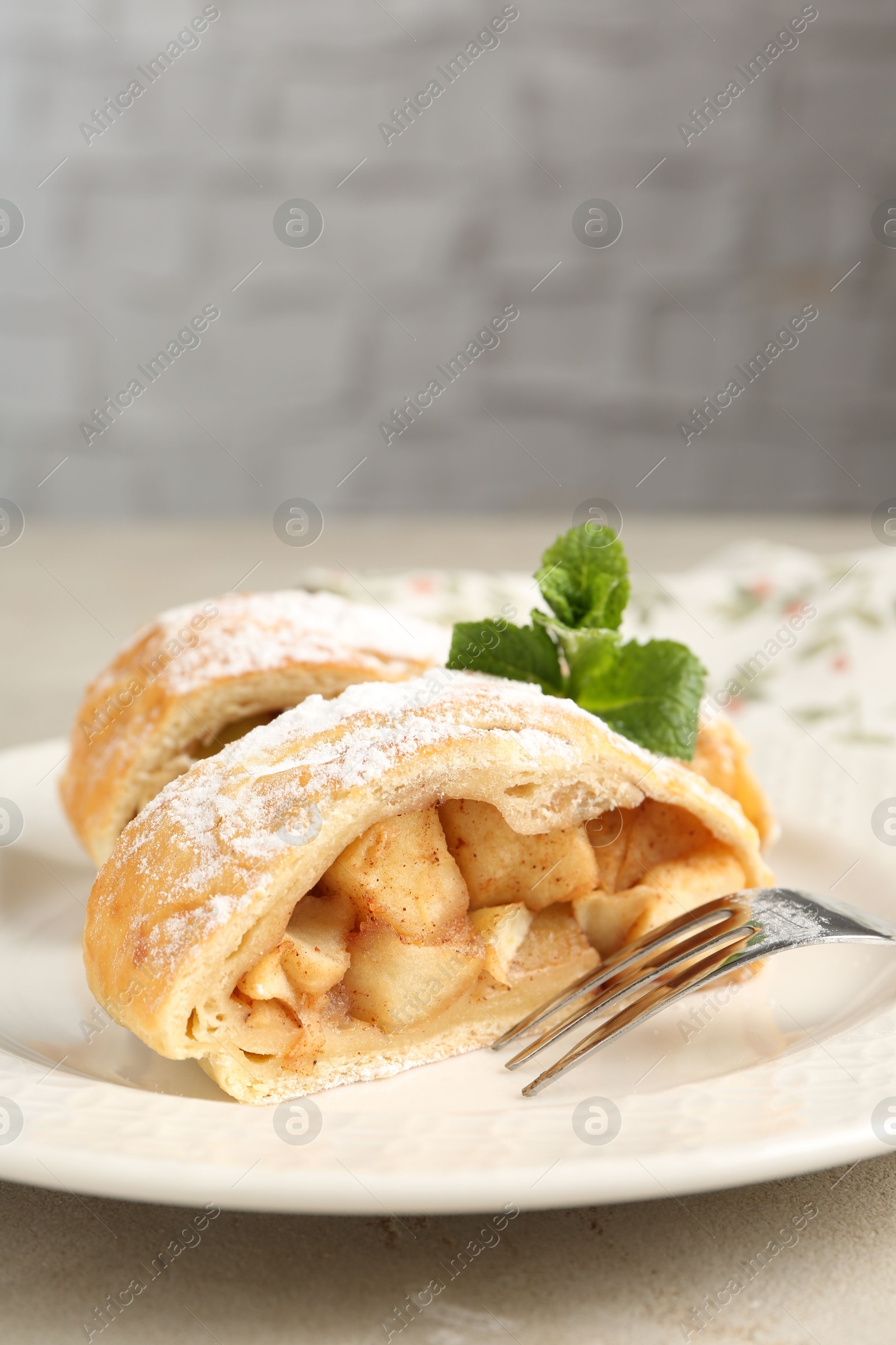 Photo of Pieces of tasty apple strudel with powdered sugar, mint and fork on grey textured table, closeup