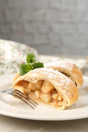 Pieces of tasty apple strudel with powdered sugar, mint and fork on grey table, closeup