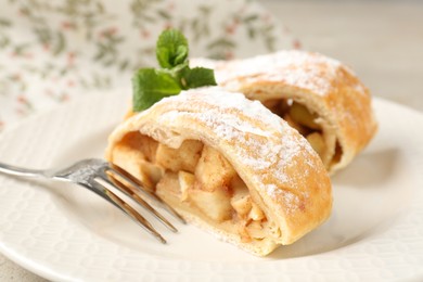 Photo of Pieces of tasty apple strudel with powdered sugar, mint and fork on grey table, closeup