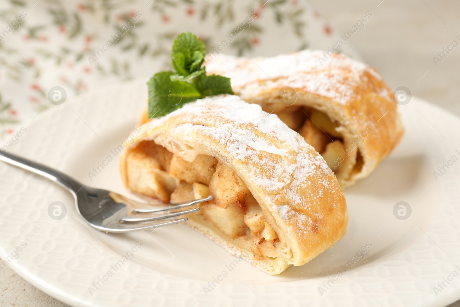 Photo of Pieces of tasty apple strudel with powdered sugar, mint and fork on grey table, closeup