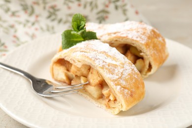 Pieces of tasty apple strudel with powdered sugar, mint and fork on grey table, closeup