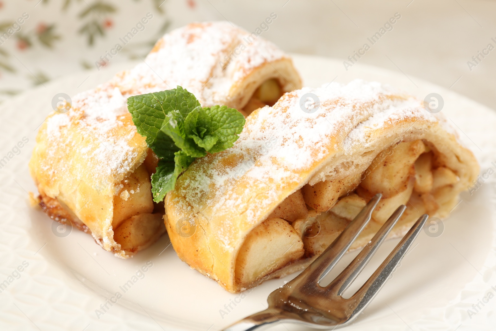 Photo of Pieces of tasty apple strudel with powdered sugar, mint and fork on table, closeup