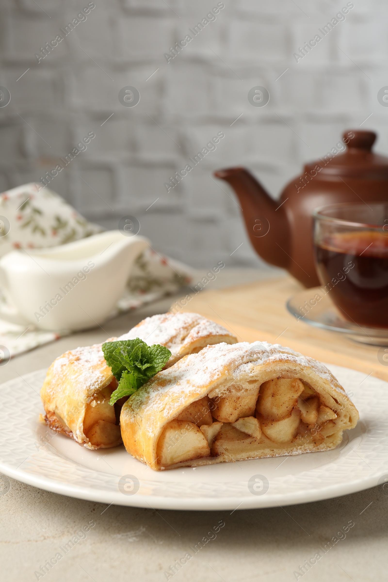 Photo of Pieces of tasty apple strudel with powdered sugar, mint and fork on grey textured table, closeup