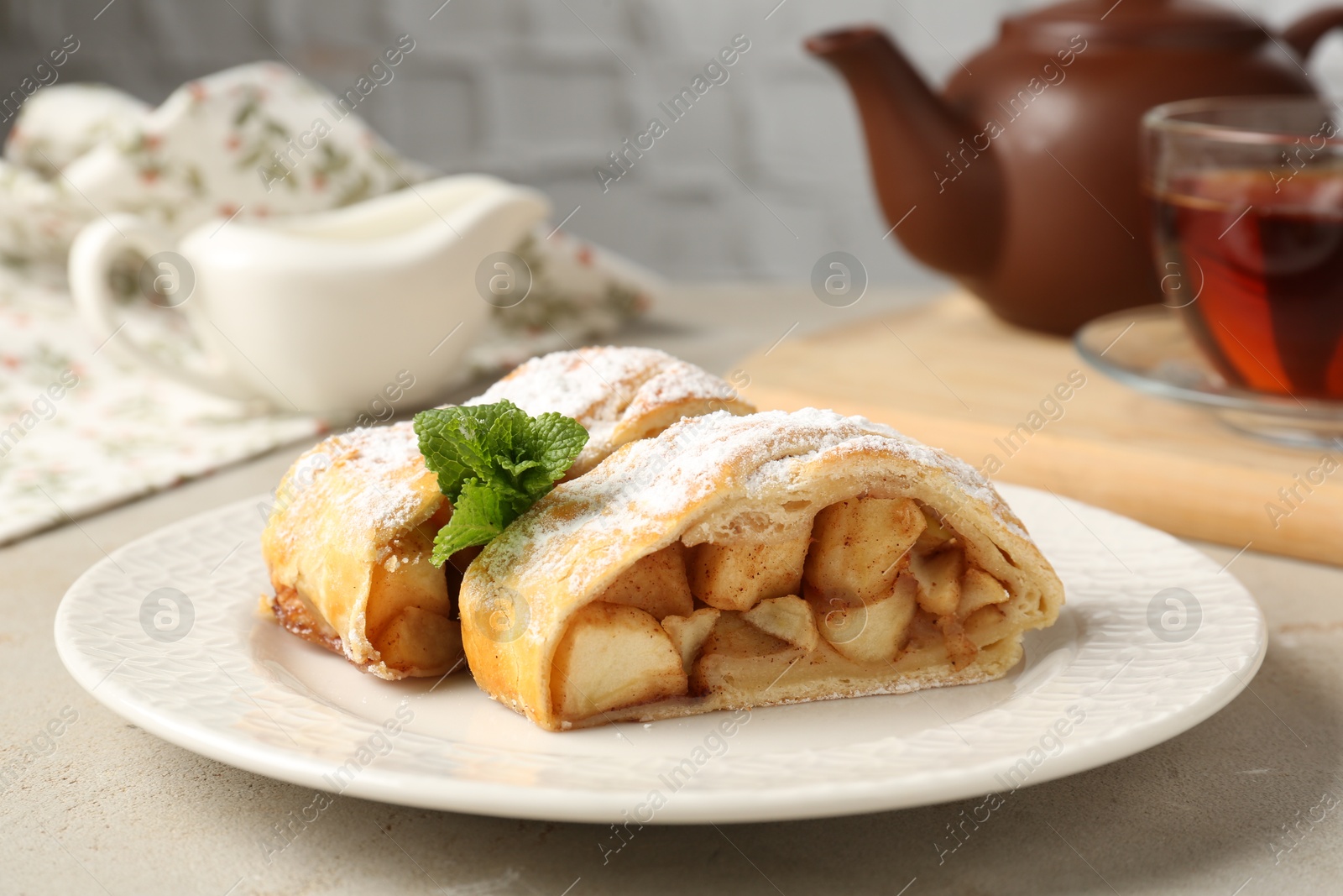 Photo of Pieces of tasty apple strudel with powdered sugar and mint on grey textured table, closeup