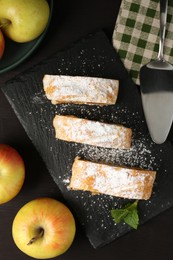 Pieces of tasty apple strudel with powdered sugar, mint and fruits on black wooden table, flat lay