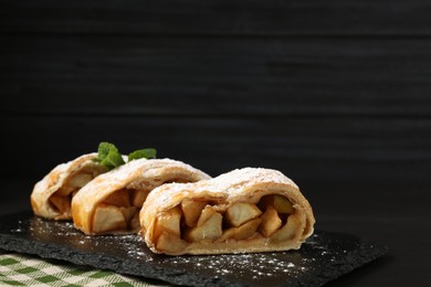 Pieces of tasty apple strudel with powdered sugar and mint on black table, closeup. Space for text