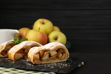 Photo of Pieces of tasty apple strudel with powdered sugar and mint on black table, closeup. Space for text