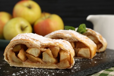 Pieces of tasty apple strudel with powdered sugar and mint on table, closeup