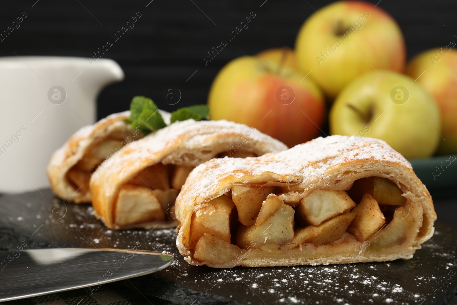 Photo of Pieces of tasty apple strudel with powdered sugar and mint on table, closeup