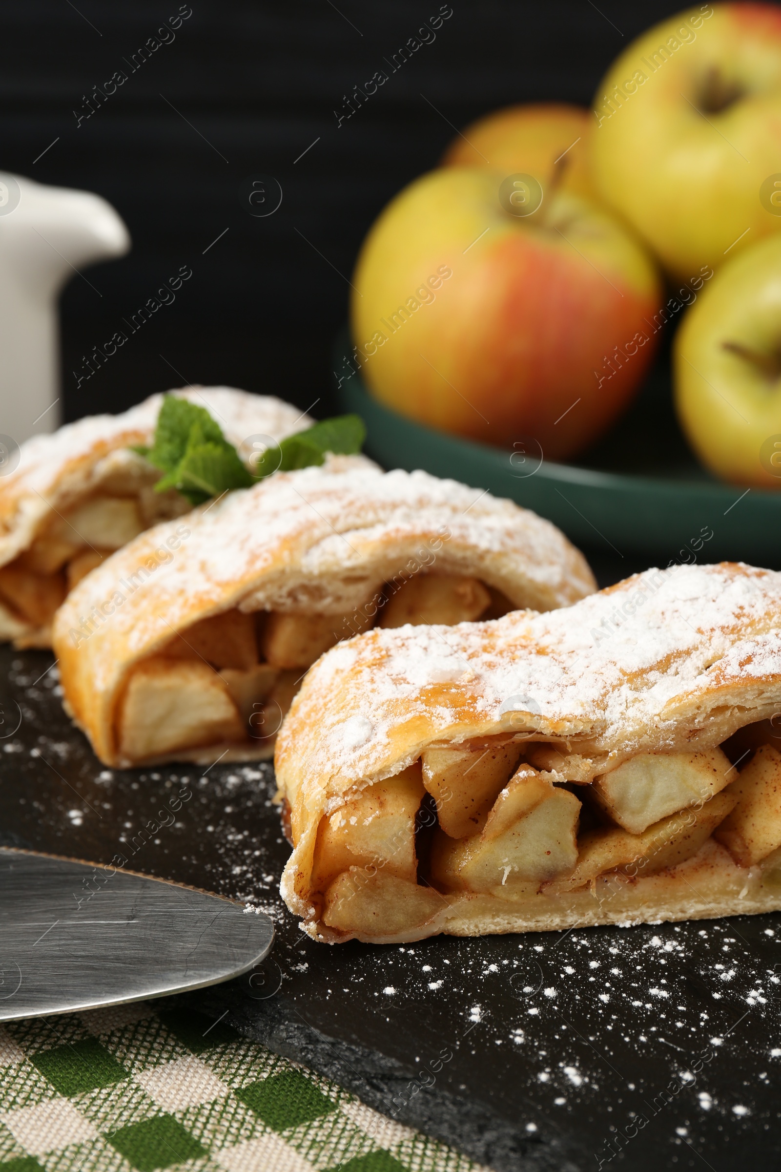 Photo of Pieces of tasty apple strudel with powdered sugar and mint on table, closeup