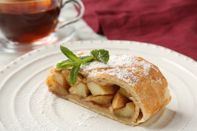 Photo of Piece of tasty apple strudel with powdered sugar and mint on table, closeup