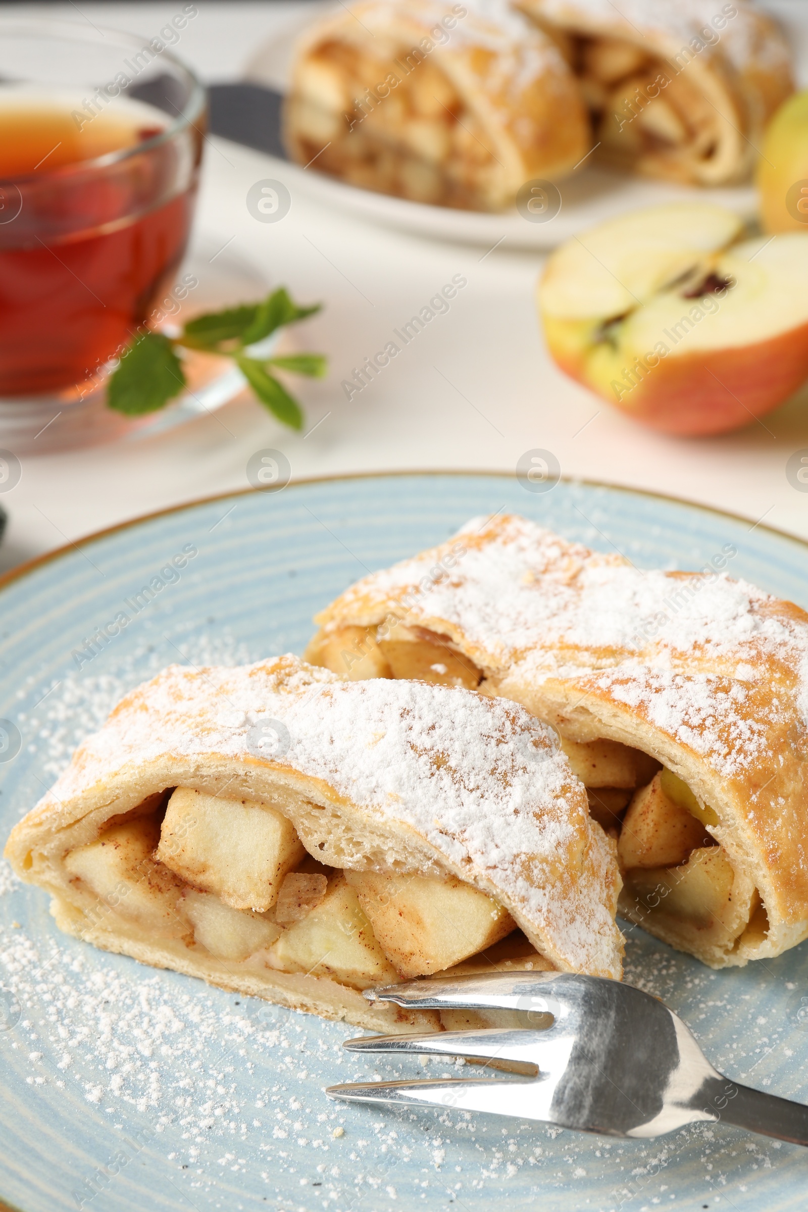 Photo of Pieces of tasty apple strudel with powdered sugar and fork on white table, closeup