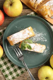 Photo of Pieces of tasty apple strudel with powdered sugar, mint, fruits and fork on wooden table, flat lay