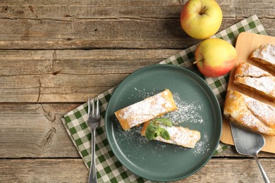 Photo of Pieces of tasty apple strudel with powdered sugar, mint and fruits on wooden table, flat lay. Space for text