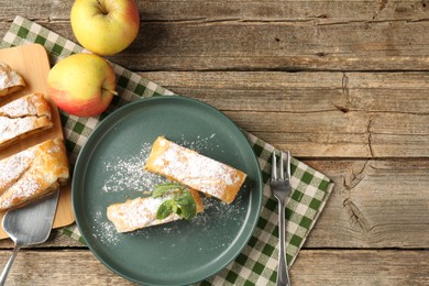 Photo of Pieces of tasty apple strudel with powdered sugar, mint and fruits on wooden table, flat lay. Space for text