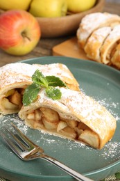 Photo of Pieces of tasty apple strudel with powdered sugar, mint and fork on table, closeup