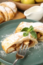 Photo of Pieces of tasty apple strudel with powdered sugar, mint and fork on table, closeup