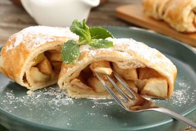 Photo of Pieces of tasty apple strudel with powdered sugar, mint and fork on table, closeup