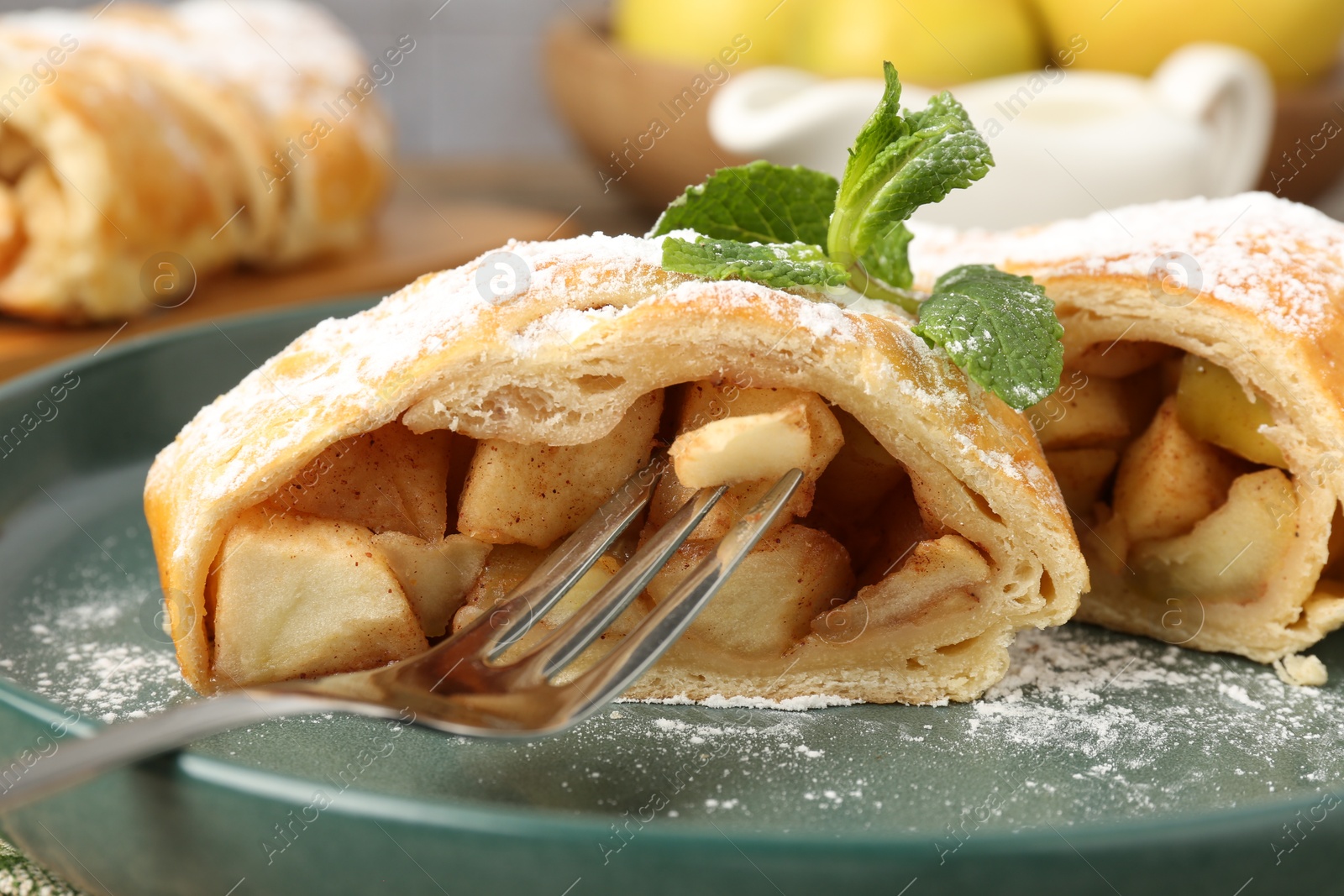 Photo of Pieces of tasty apple strudel with powdered sugar, mint and fork on table, closeup