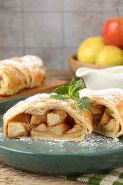 Photo of Pieces of tasty apple strudel with powdered sugar and mint on wooden table, closeup