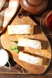 Photo of Pieces of tasty apple strudel with powdered sugar and mint on wooden table, flat lay