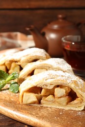 Photo of Pieces of tasty apple strudel with powdered sugar and mint on wooden table, closeup