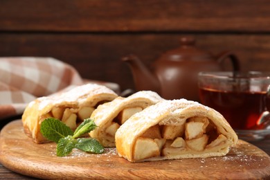 Photo of Pieces of tasty apple strudel with powdered sugar and mint on wooden table, closeup