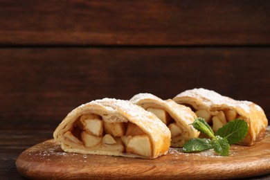 Photo of Pieces of tasty apple strudel with powdered sugar and mint on wooden table, closeup. Space for text