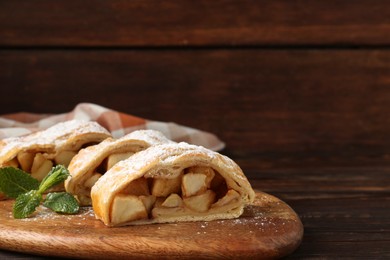 Photo of Pieces of tasty apple strudel with powdered sugar and mint on wooden table, closeup. Space for text