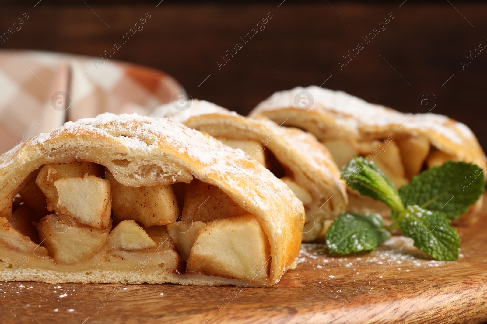 Photo of Pieces of tasty apple strudel with powdered sugar and mint on wooden board, closeup