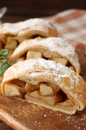 Photo of Pieces of tasty apple strudel with powdered sugar on wooden board, closeup