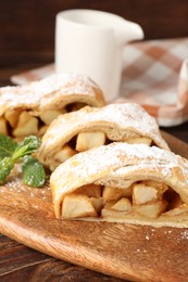 Photo of Pieces of tasty apple strudel with powdered sugar and mint on wooden table, closeup