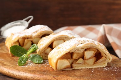 Photo of Pieces of tasty apple strudel with powdered sugar and mint on wooden table, closeup