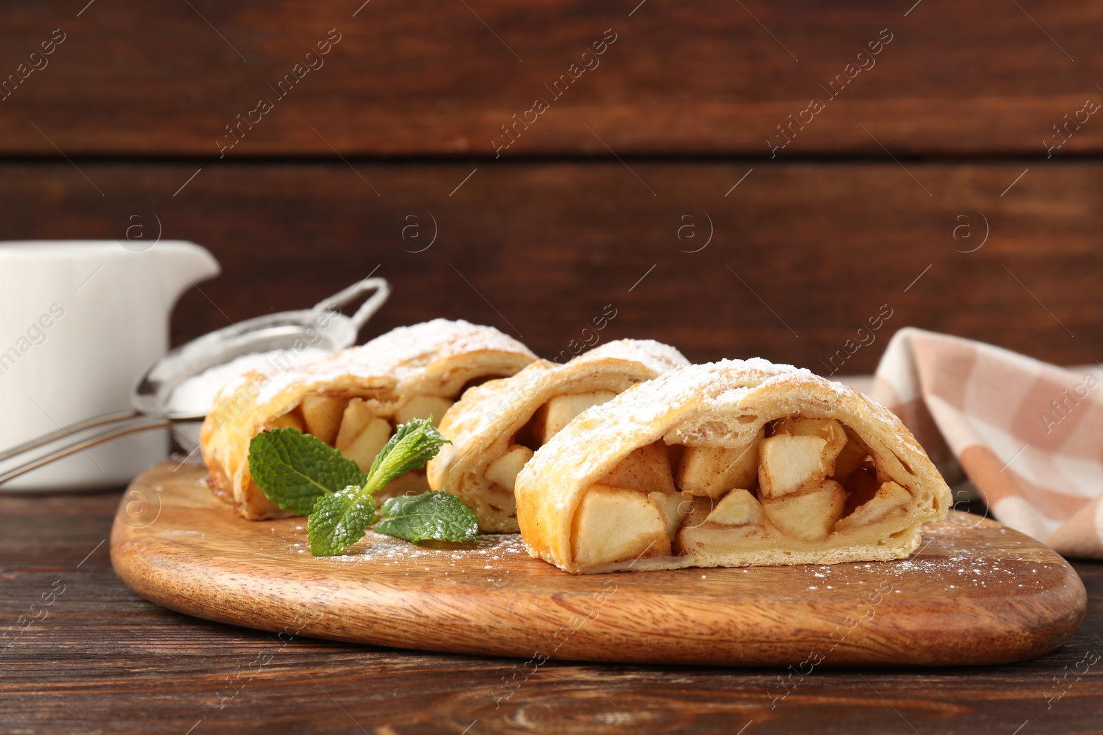 Photo of Pieces of tasty apple strudel with powdered sugar and mint on wooden table, closeup