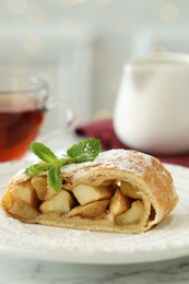 Photo of Piece of tasty apple strudel with powdered sugar and mint on white marble table, closeup