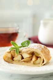 Photo of Piece of tasty apple strudel with powdered sugar and mint on white marble table, closeup