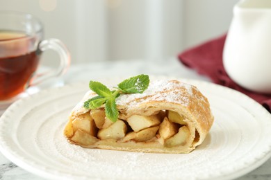 Photo of Piece of tasty apple strudel with powdered sugar and mint on table, closeup