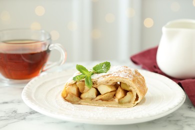 Photo of Piece of tasty apple strudel with powdered sugar and mint on white marble table, closeup