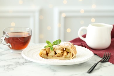 Photo of Piece of tasty apple strudel served with tea on white marble table, closeup