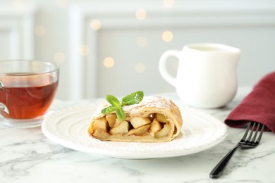 Photo of Piece of tasty apple strudel served with tea on white marble table, closeup