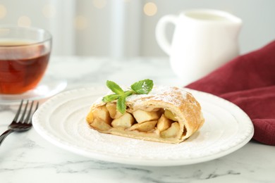 Photo of Piece of tasty apple strudel served with tea on white marble table, closeup