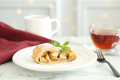 Photo of Piece of tasty apple strudel served with tea on white marble table, closeup