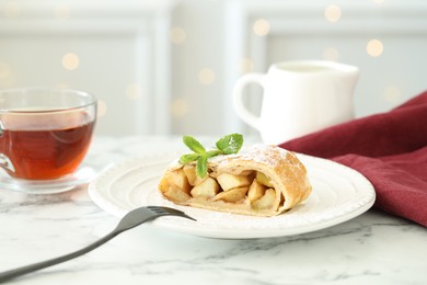 Photo of Piece of tasty apple strudel served with tea on white marble table, closeup