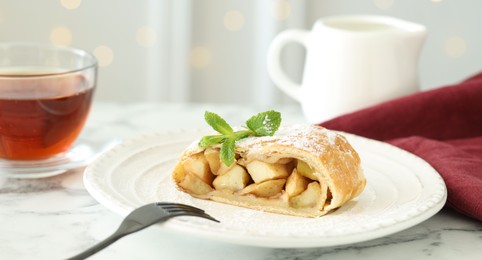 Photo of Piece of tasty apple strudel served with tea on white marble table, closeup